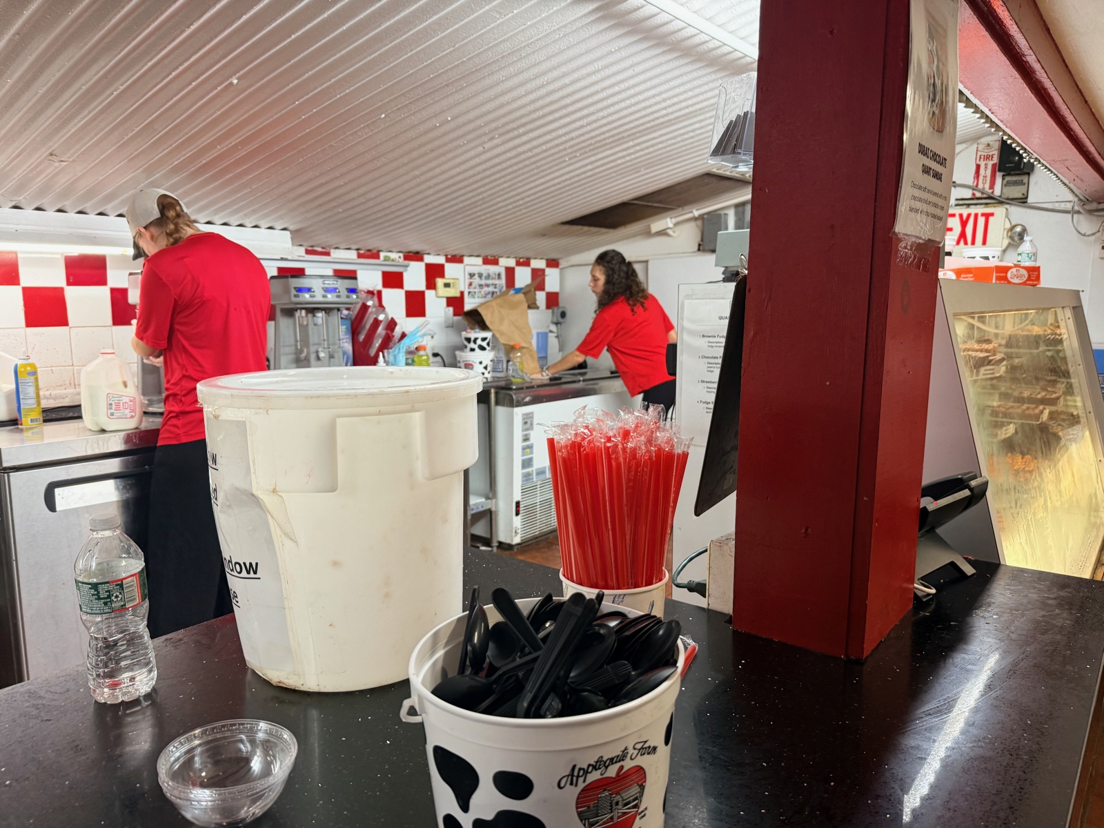 Behind the counter at Applegate Farm, red and white tile, straws in a cup, the crew scooping