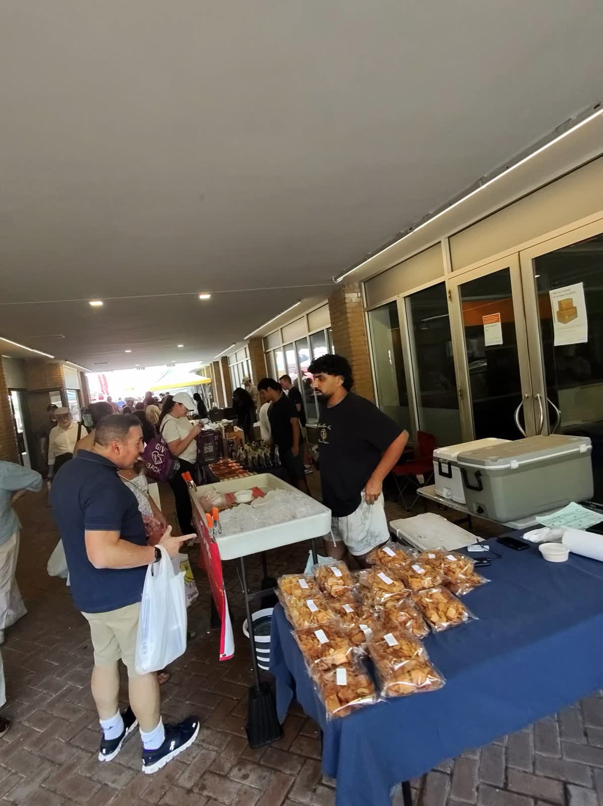 A vendor plates fresh fruit samples on skewers at a farmers market table while shoppers wait